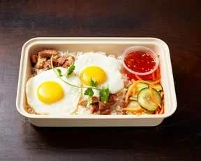 Asian Box breakfast, featuring two fried eggs on rice, cucumber and carrot salad and a side sauce.
